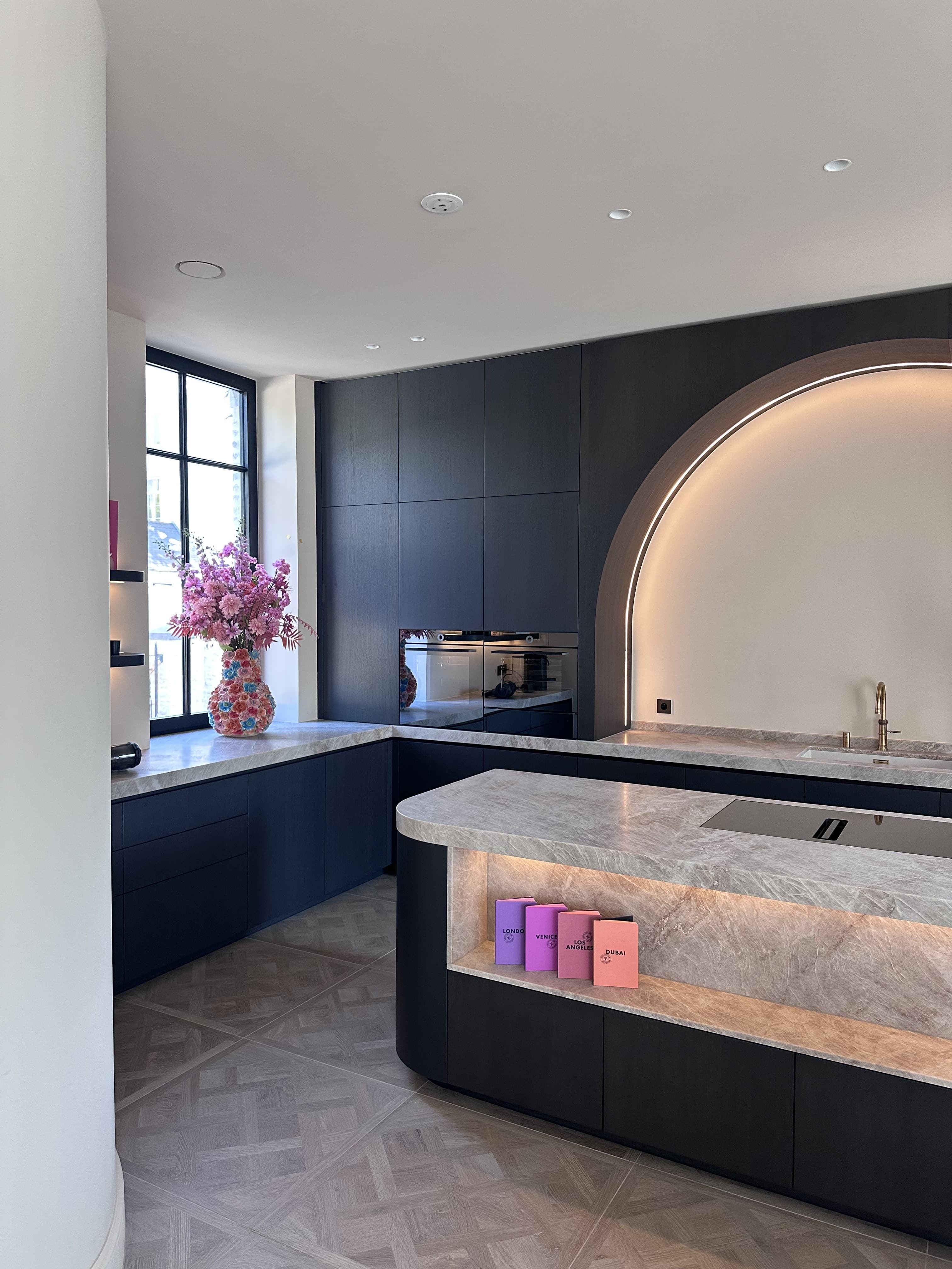 Keuken met matzwarte kastenwand en natuurstenen werkblad, met een verlichte boognis in een gladde minerale wandafwerking.
